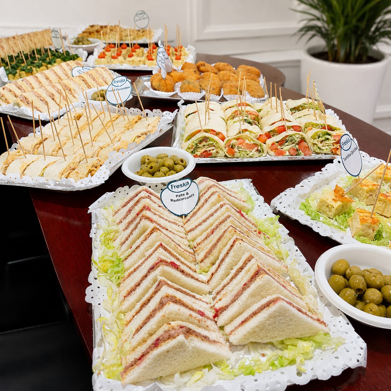 Catering table of finger sandwiches, wraps and olives labelled with Freska name cards