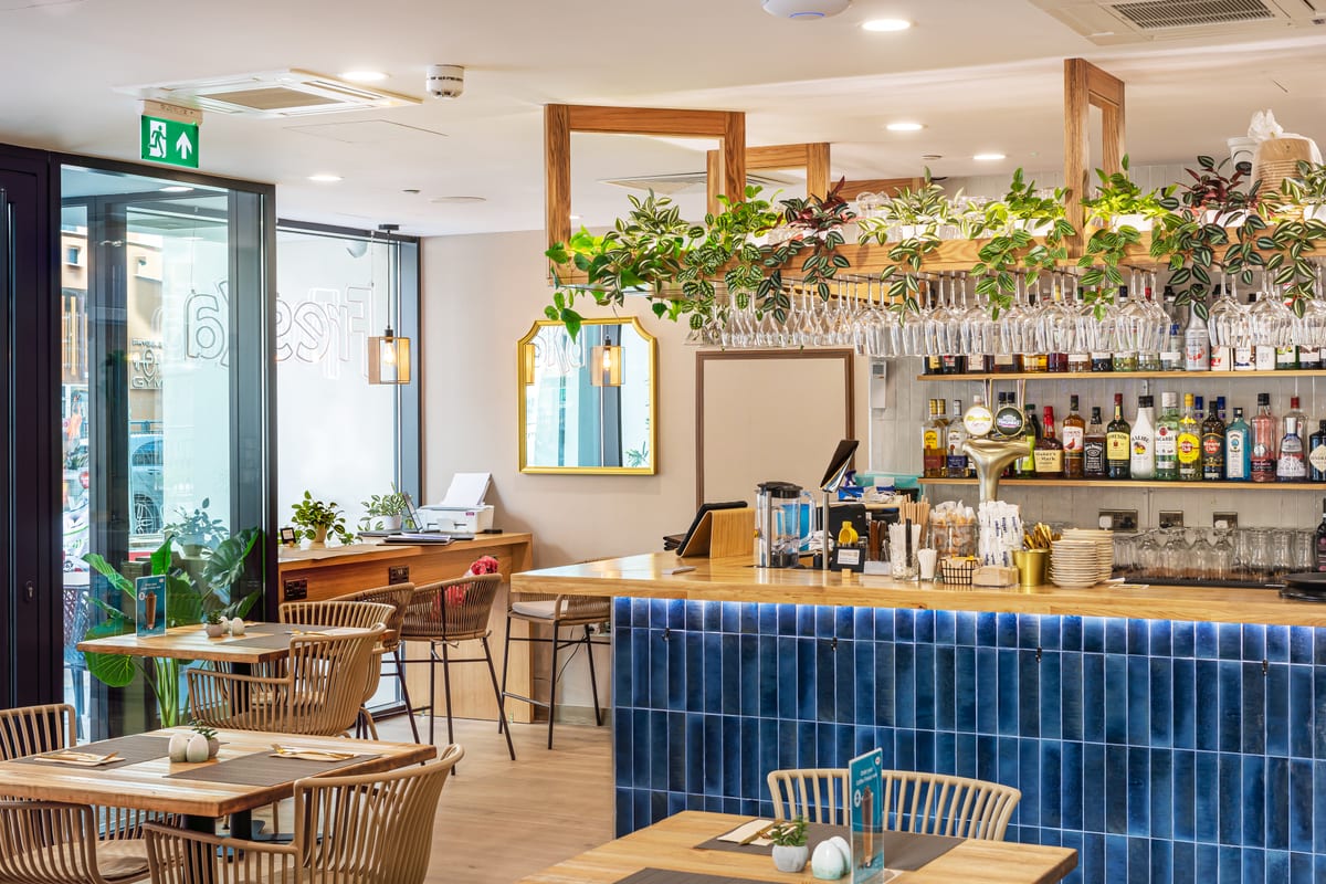 Freska E1 dining area with a wooden bar counter, blue tiled front and hanging plants