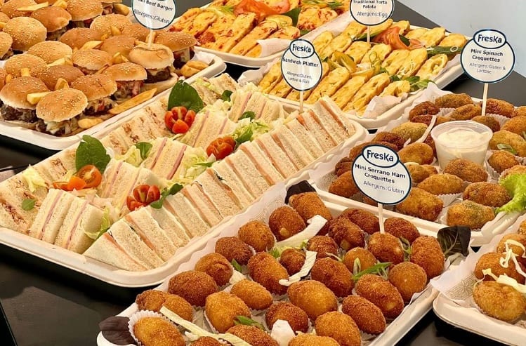Long catering table of canapés and pastries set up in an office reception area