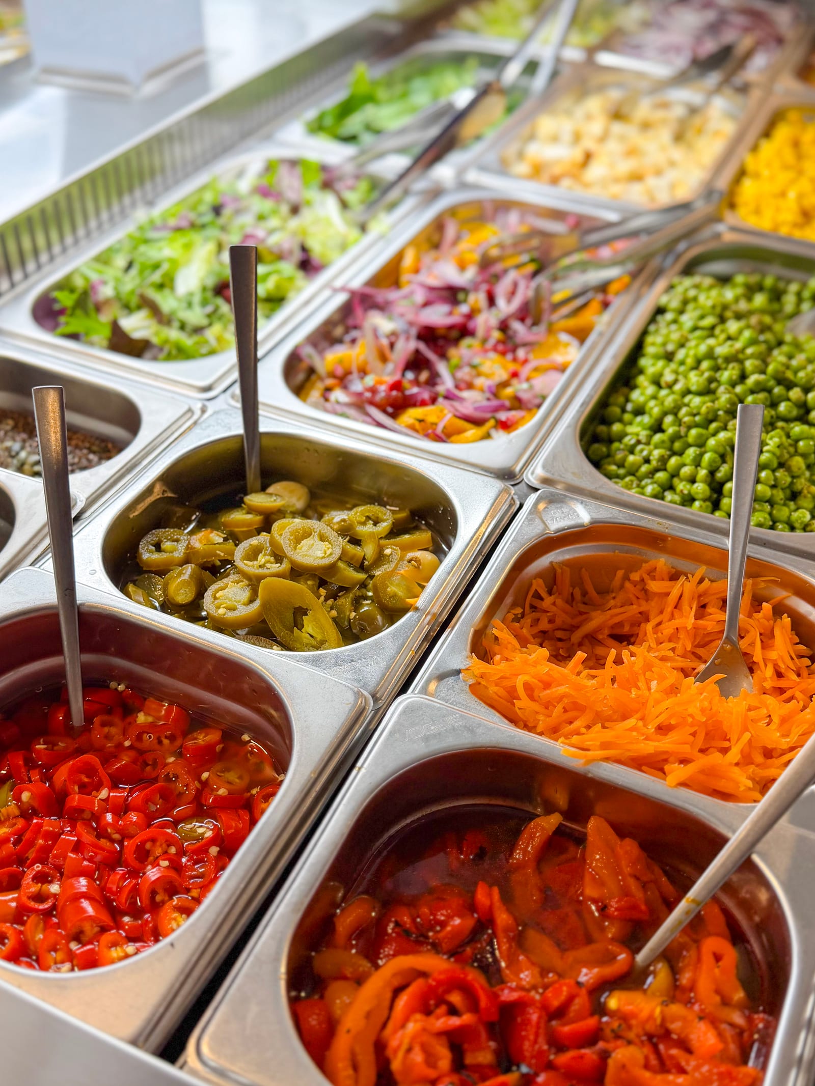 Salad bar trays of jalapeños, roasted peppers, olives and shredded carrot