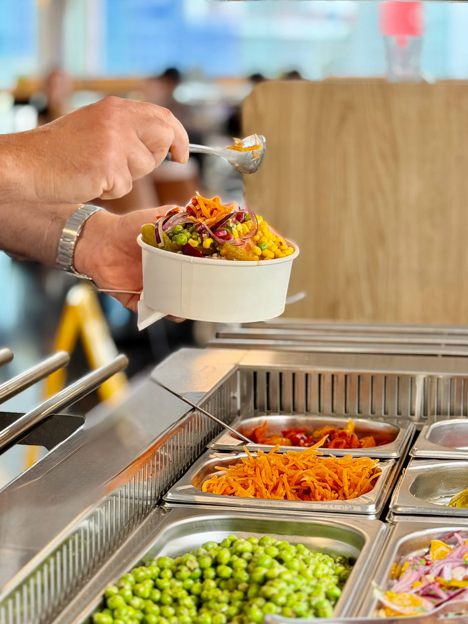 Hand adding sweetcorn, carrot and beetroot toppings to a fresh salad bowl