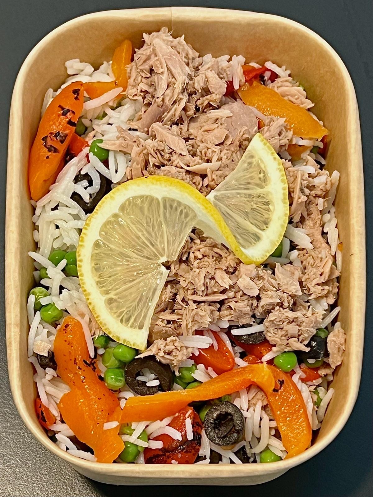 Meal-prep box of tuna, rice, peas, olives and roasted peppers with a lemon wedge