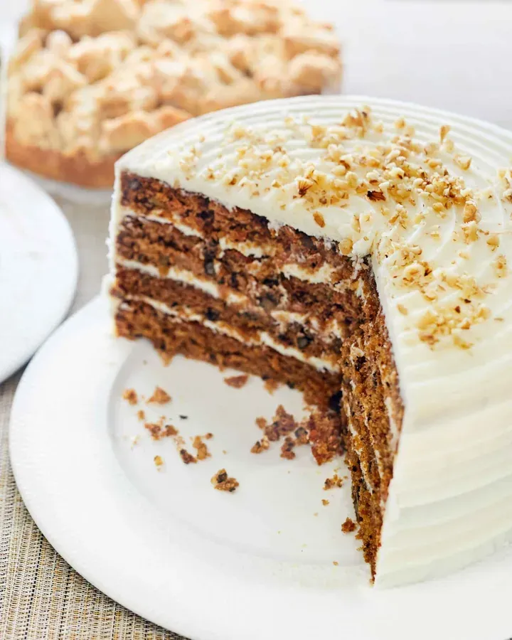 Sliced layered carrot cake topped with cream cheese frosting and chopped walnuts