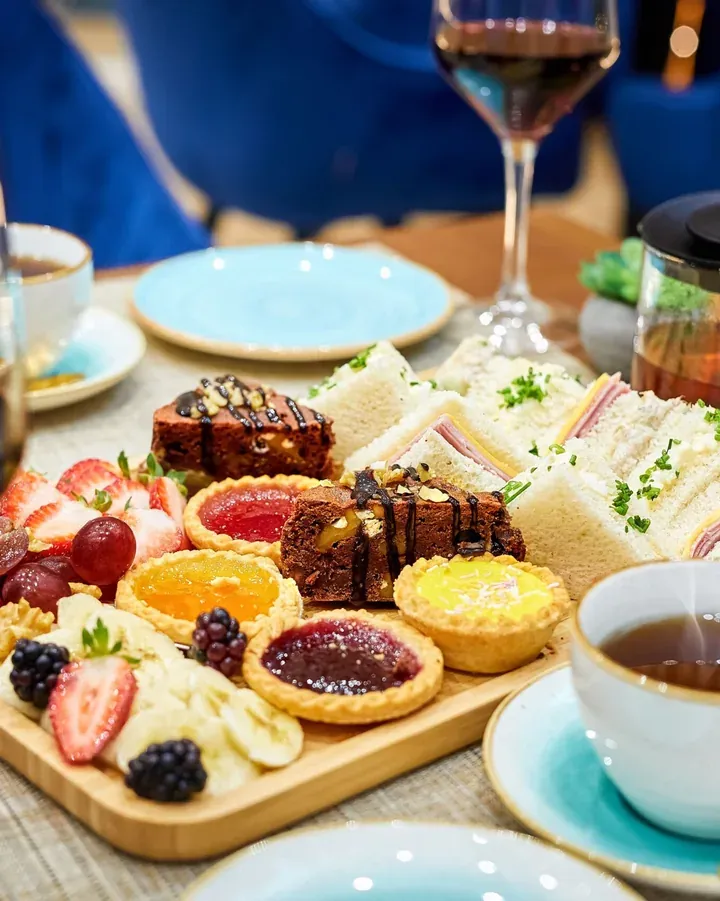 Afternoon tea spread of brownies, fruit tarts, finger sandwiches, fresh fruit and a glass of wine