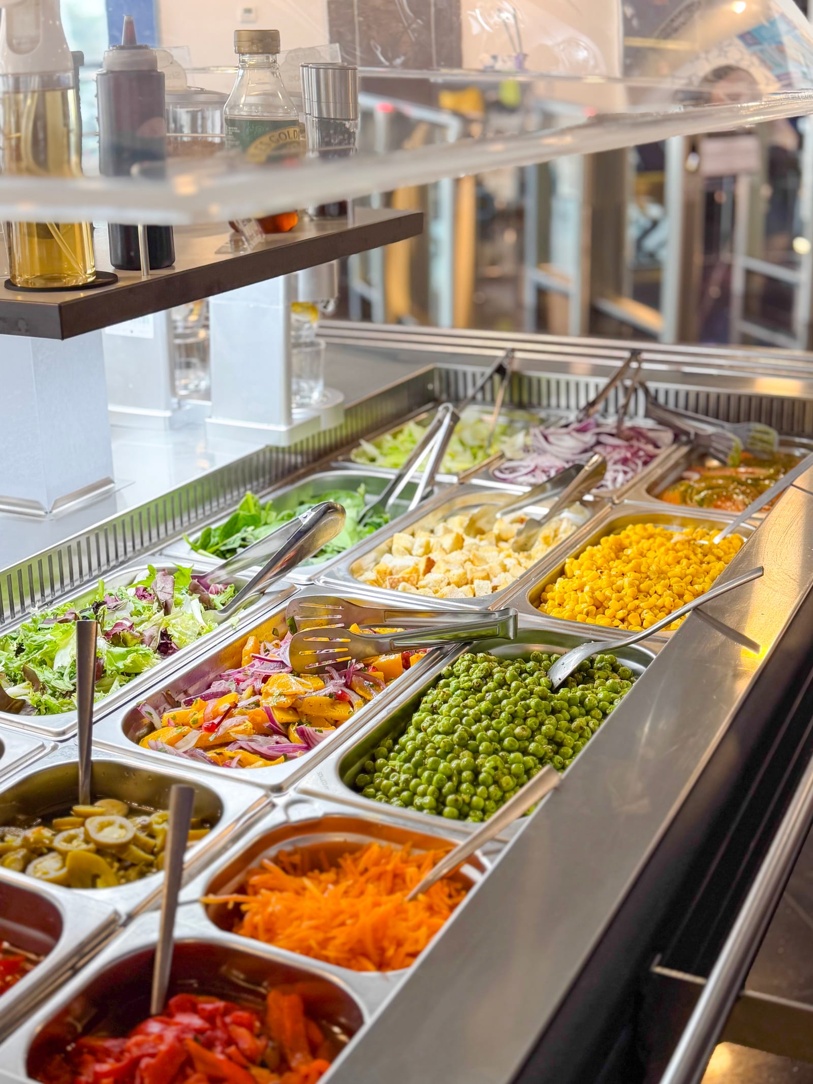 Salad bar trays of leafy greens, roasted peppers, sweetcorn and peas